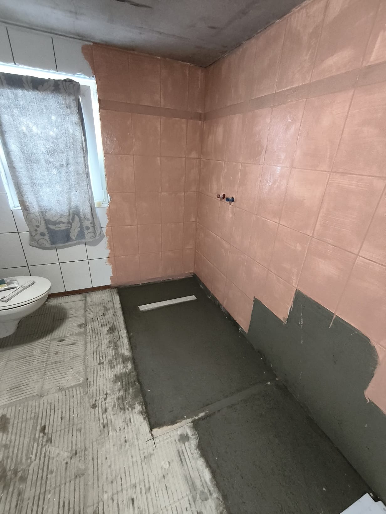 Wyrównywanie podłoża w łazience w Warszawie. Częściowo położone płytki na ścianach, wylewka na podłodze, widoczny odpływ liniowy. Etap prac przygotowawczych.