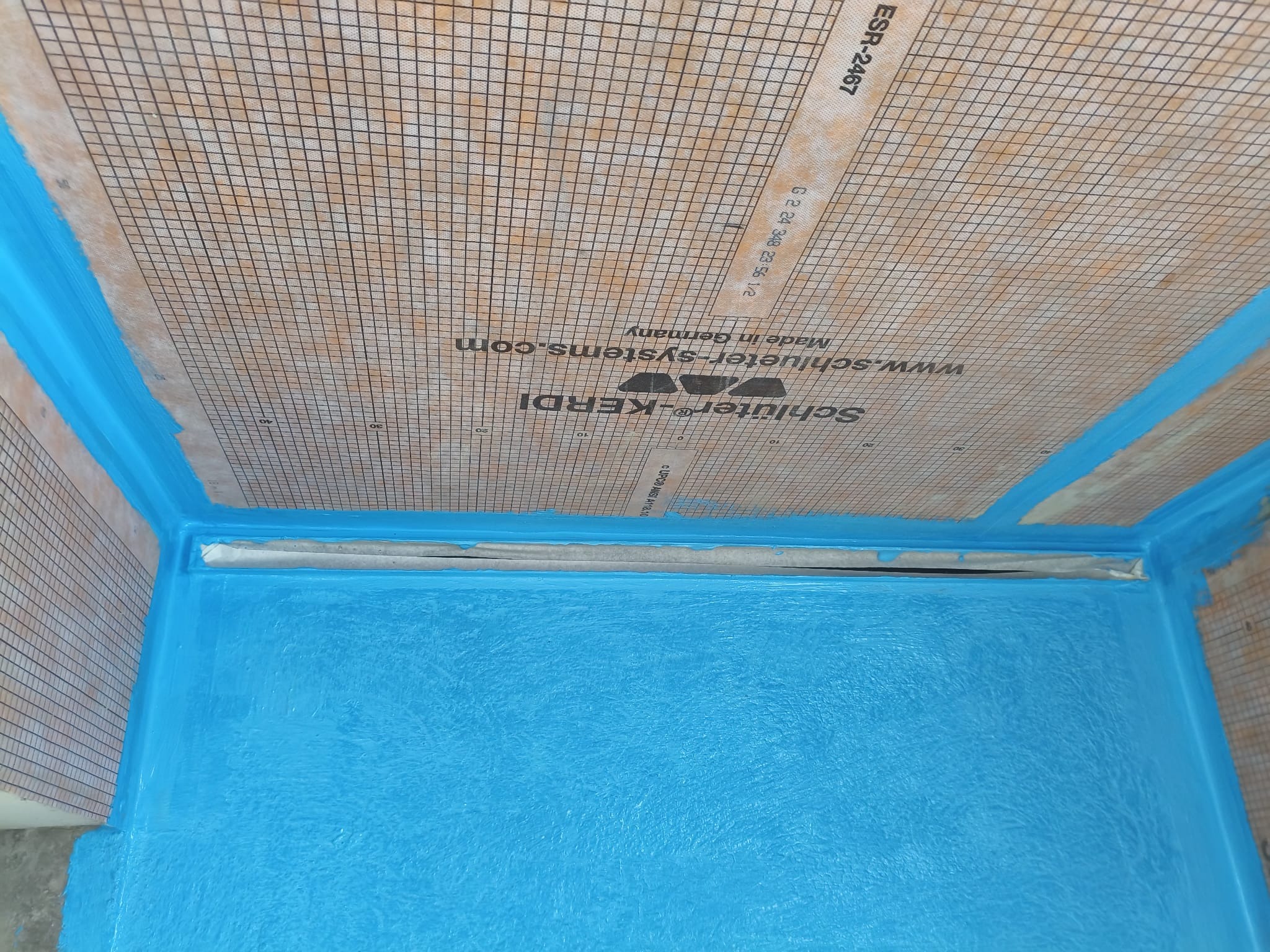 Hydroizolacja brodzika z odpływem liniowym, zabezpieczona niebieską folią w płynie. Widoczna mata uszczelniająca na ścianach. Schluter Kerdi.