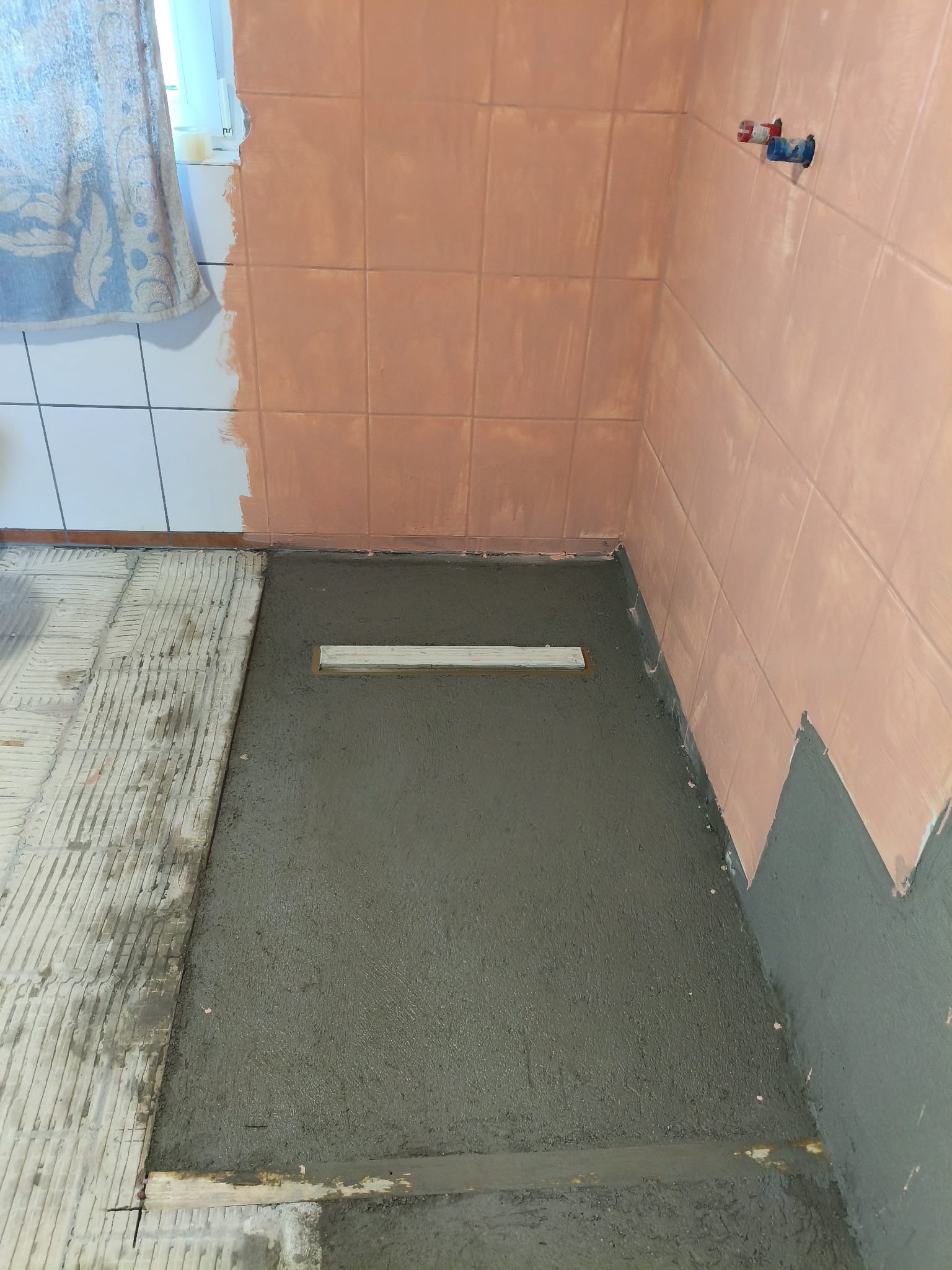 Wyrównywanie podłoża w łazience wylewką samopoziomującą, widoczny odpływ liniowy. Częściowo położone płytki na ścianach. Przygotowanie do dalszych prac wykończeniowych.