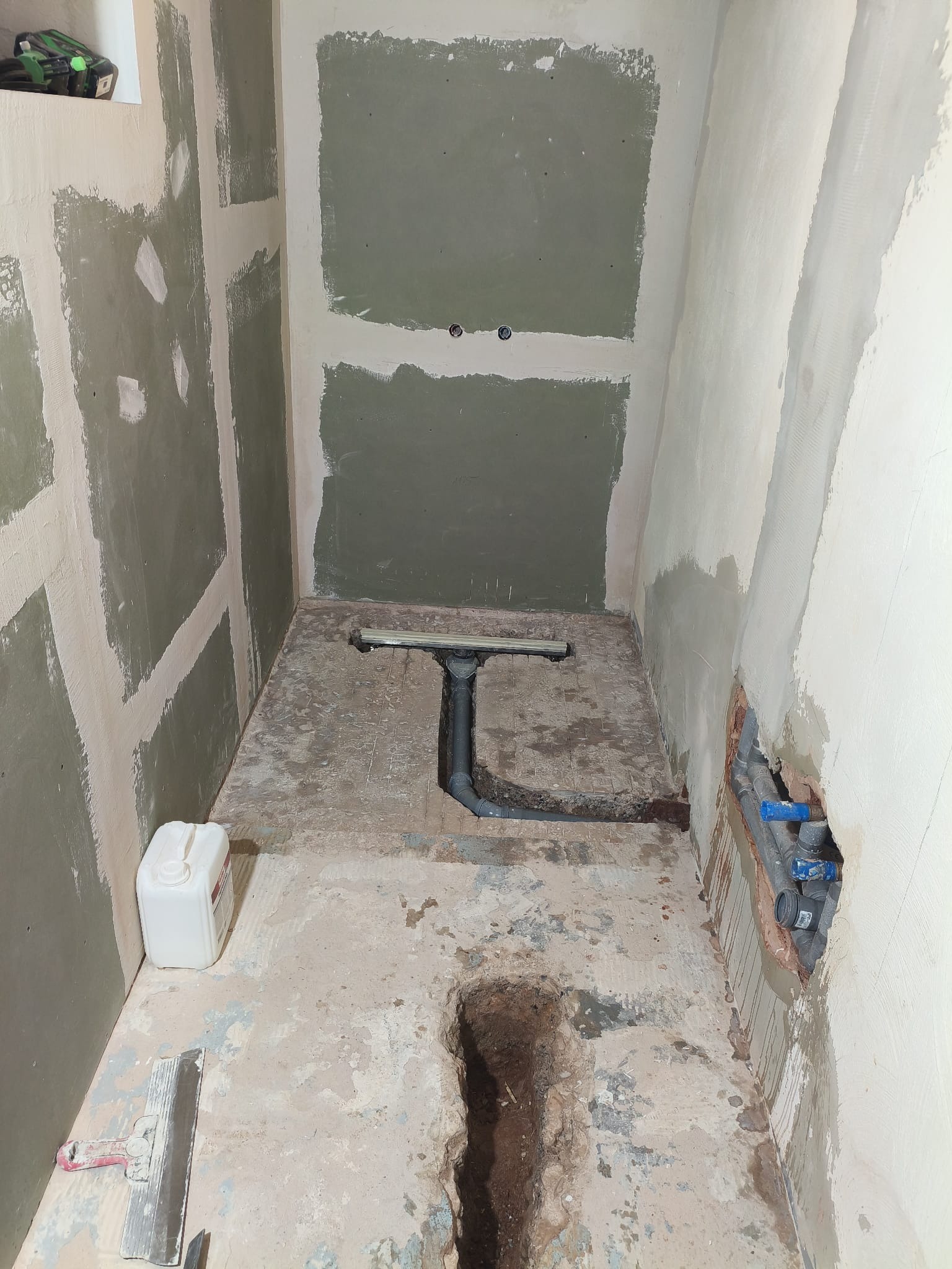 Łazienka w trakcie prac: widoczne płyty karton-gips na ścianach, odpływ liniowy w posadzce, instalacja wodna w ścianie. Etap przygotowania do dalszych prac wykończeniowych.