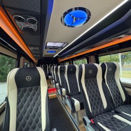 Premium Transfer - Krystian Błotniak - Wnętrze luksusowego busa Mercedes z pikowanymi skórzanymi fotelami w kolorach czerni i beżu, oświetleniem LED i logo marki na zagłówkach.