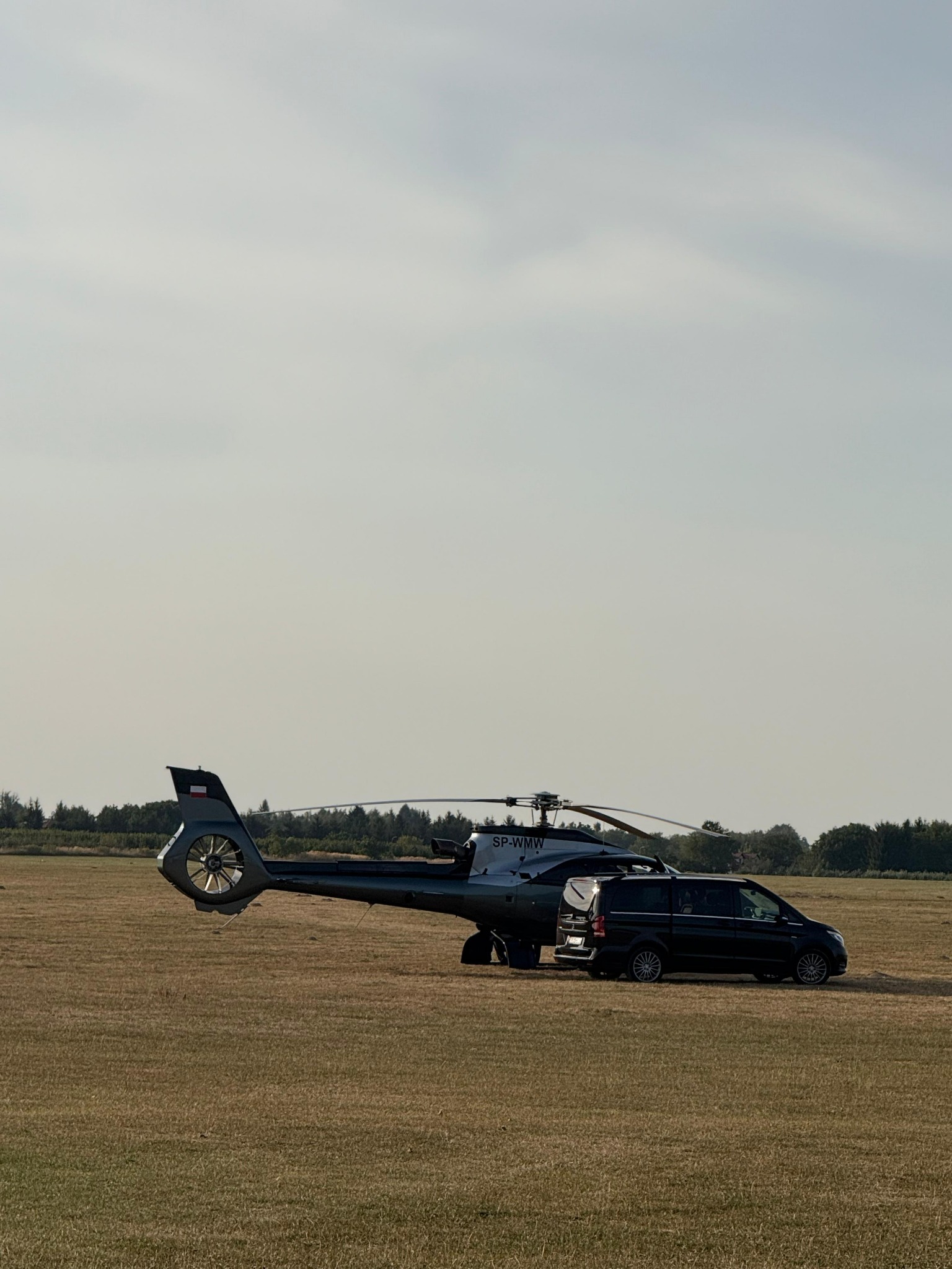 Czarny helikopter SP-WMW i czarny van Mercedes V-klasy na trawiastym lotnisku, transfer VIP, luksusowy transport.