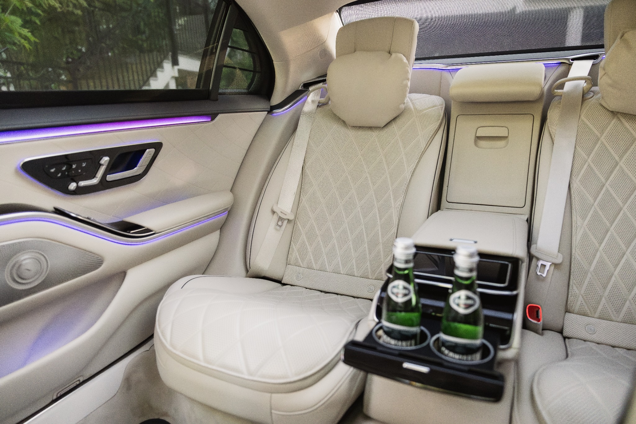 Luksusowe wnętrze samochodu z beżową skórzaną tapicerką, podświetleniem LED i butelkami wody na tylnym siedzeniu. Widok z perspektywy pasażera.