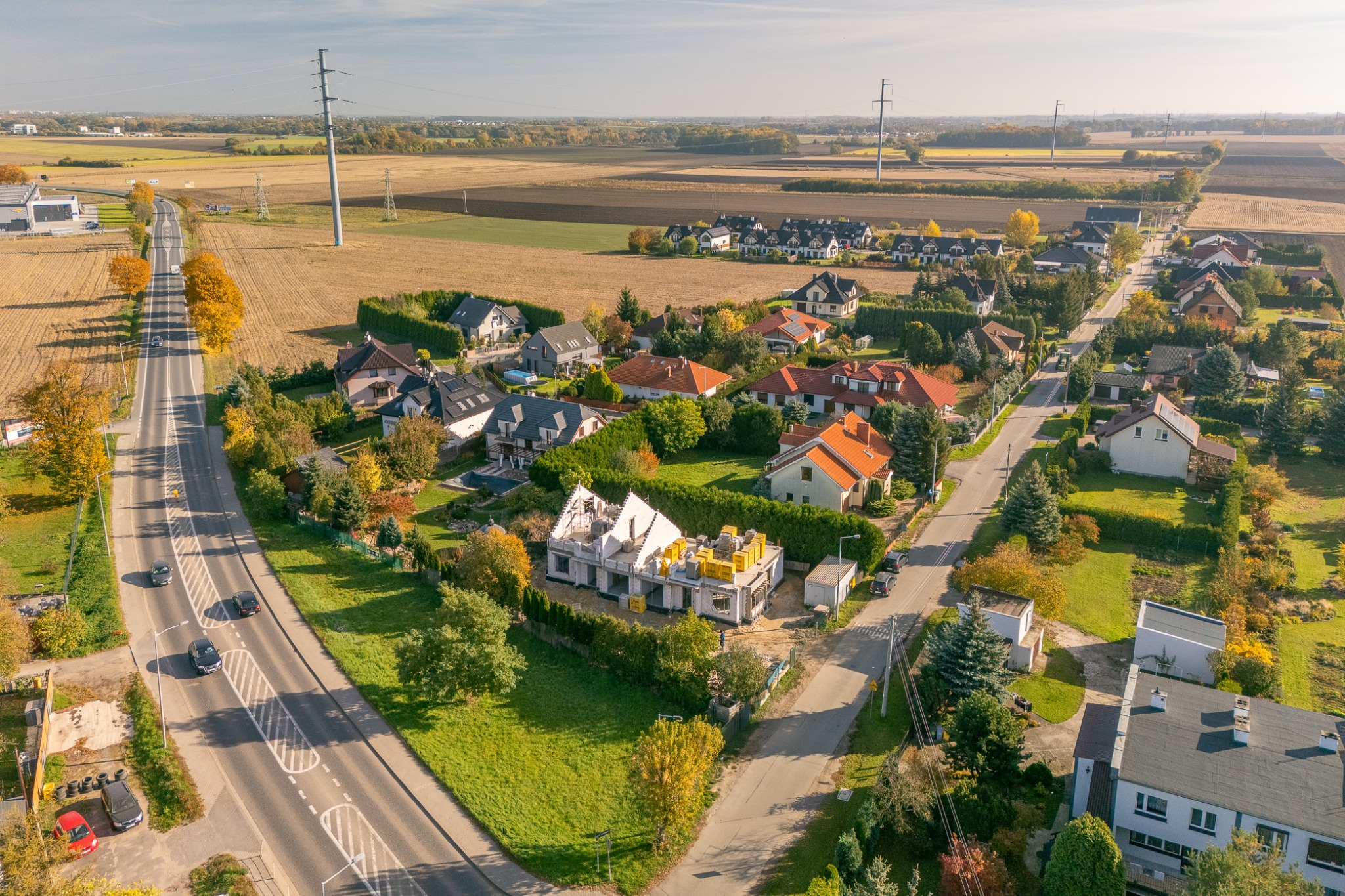 Aerial widok na budowę domu jednorodzinnego w stanie surowym otwartej, z żółtymi bloczkami na dachu, w otoczeniu zieleni i zabudowy mieszkalnej.