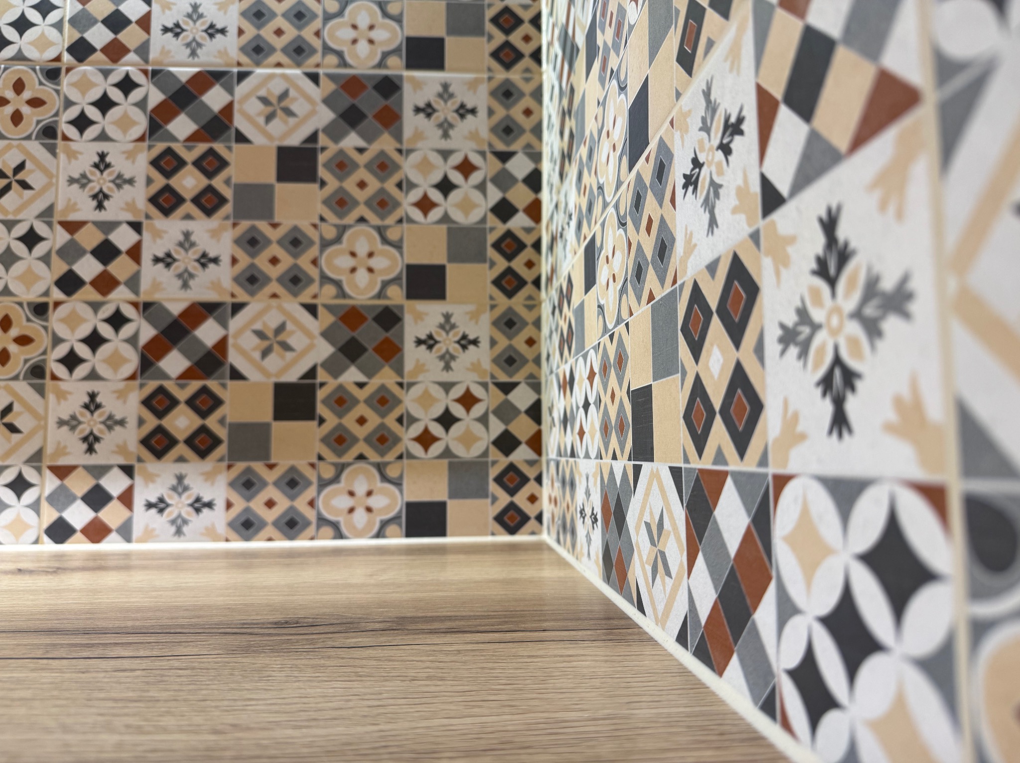 Fragment wykończonej ściany z dekoracyjnymi, wzorzystymi płytkami w odcieniach beżu, brązu i szarości, połączonej z blatem imitującym drewno. Ujęcie z niskiej perspektywy.