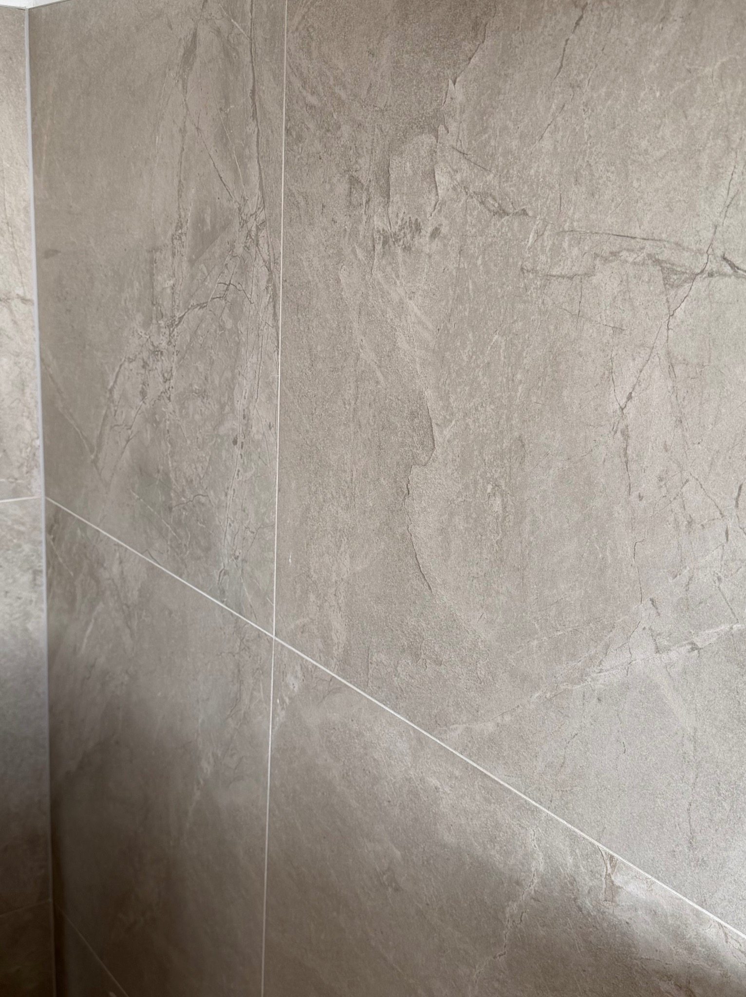 Ściana wyłożona szarymi, matowymi płytkami imitującymi kamień z delikatną fakturą i jasnymi fugami. Widok z bliska, ukazujący precyzję ułożenia.