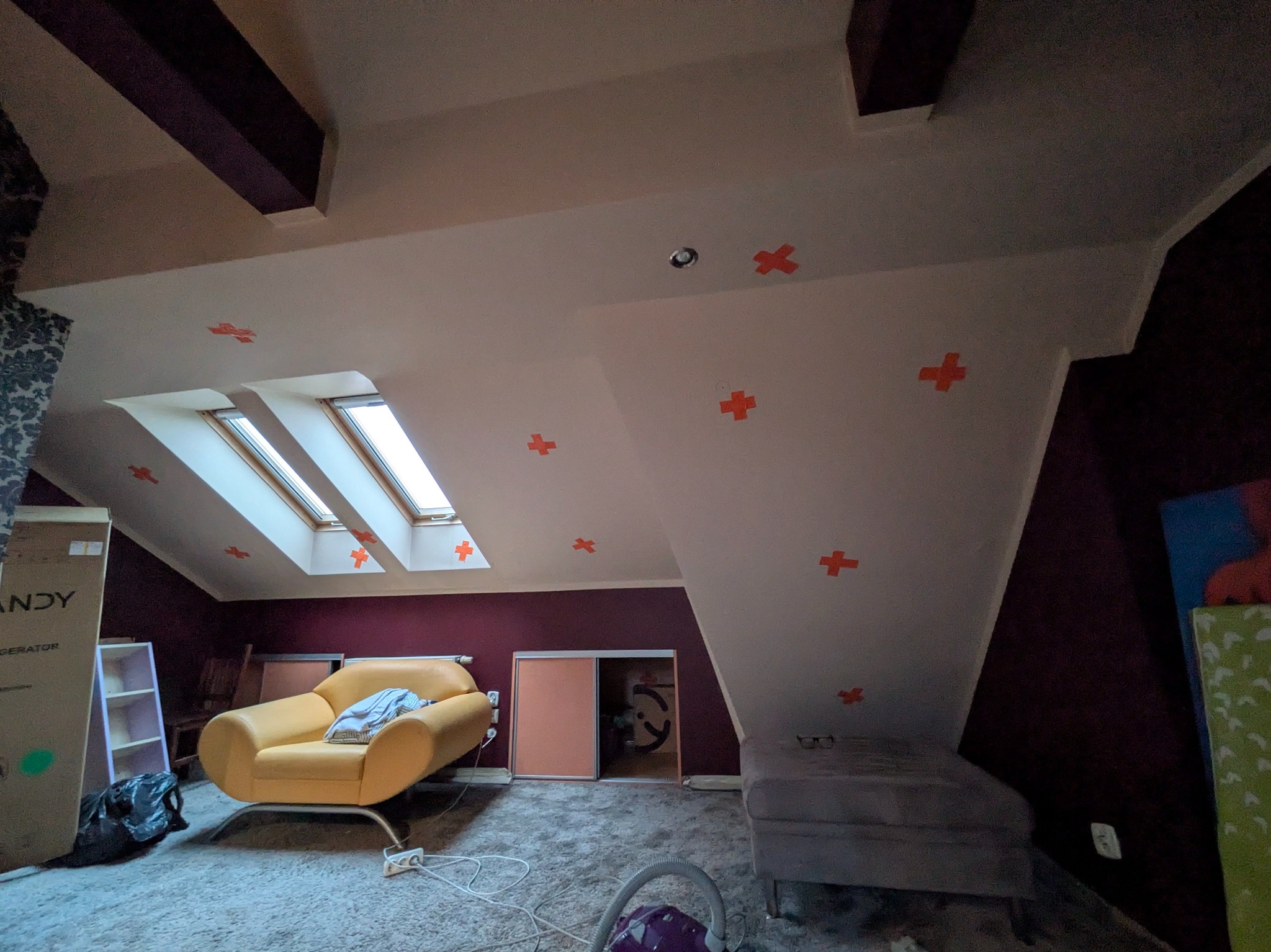 Poddasze ze skosami przed pracami: okna dachowe, czerwone krzyżyki na suficie, meble w nieładzie. Widok na przygotowane pomieszczenie przed ociepleniem.