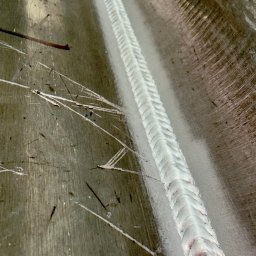 StegWeld - Szlifowana powierzchnia metalu ze świeżym, równym spoiwem spawalniczym pośrodku, widoczne drobne odpryski i rysy. Ukazany detal wykonanej pracy.