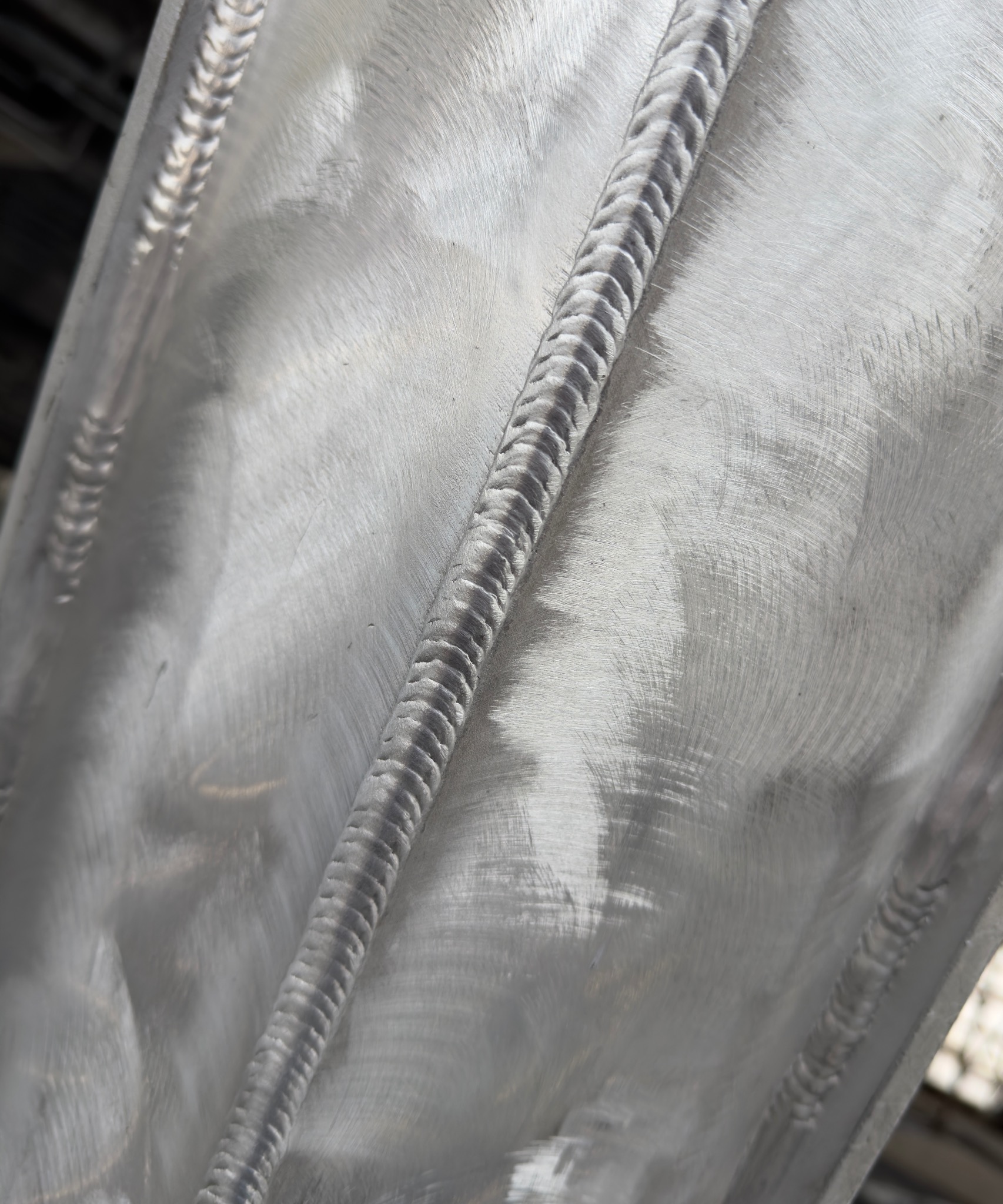 Szlifowana powierzchnia metalu z wyraźnym, precyzyjnym spoiwem spawalniczym. Widoczne ślady obróbki mechanicznej i detale spoiny.