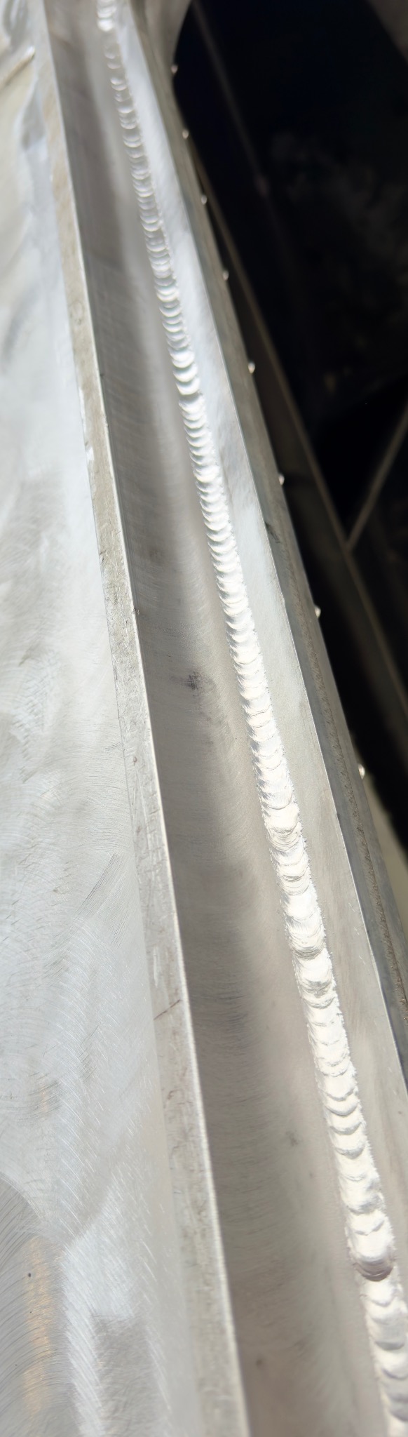 Szlifowany profil metalowy z widocznym spoiną, ukazujący precyzję wykonania i gładką powierzchnię. Detal obróbki metalu z bliska.