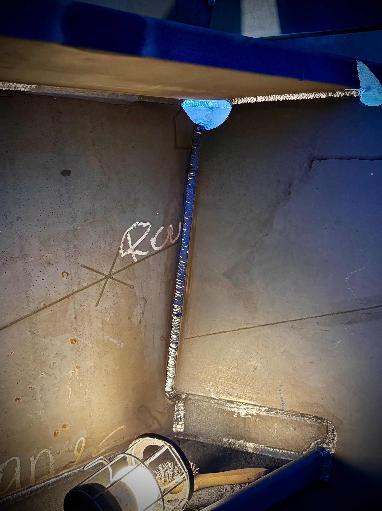 Wnętrze konstrukcji stalowej z widocznymi spawami, oznaczeniami i lampą roboczą. Detal wykonania z bliska, ukazujący precyzję łączeń i surowość materiału.