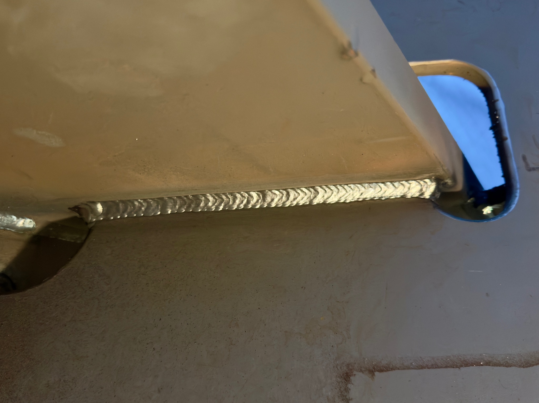 Szczegółowe zbliżenie na precyzyjne spawy łączące metalowe elementy konstrukcji, widoczne ślady obróbki i otwór w elemencie. Jasne oświetlenie podkreśla jakość wykonania.