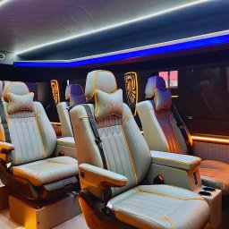 POLONIA BUS Busy do Holandii, Niemiec, Belgii, Szwajcarii, Włoch i Austrii - Wnętrze luksusowego busa z szarymi skórzanymi fotelami z pomarańczowymi akcentami, oświetleniem LED i dekoracyjnymi elementami na zagłówkach.