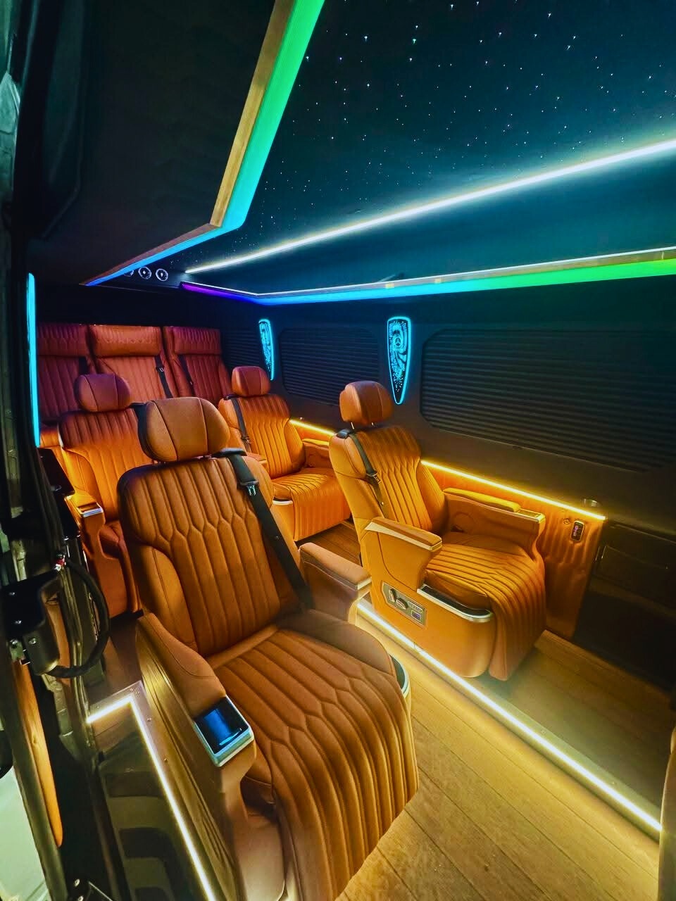 Luksusowe wnętrze busa z brązowymi skórzanymi fotelami, oświetleniem LED i podsufitką imitującą rozgwieżdżone niebo. Komfortowy transport VIP.