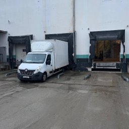 DanLogistics - Biały bus dostawczy Renault Master zaparkowany przed rampą magazynową z otwartymi wrotami. Widoczny numer rejestracyjny pojazdu i fragment logo na nadbudowie.