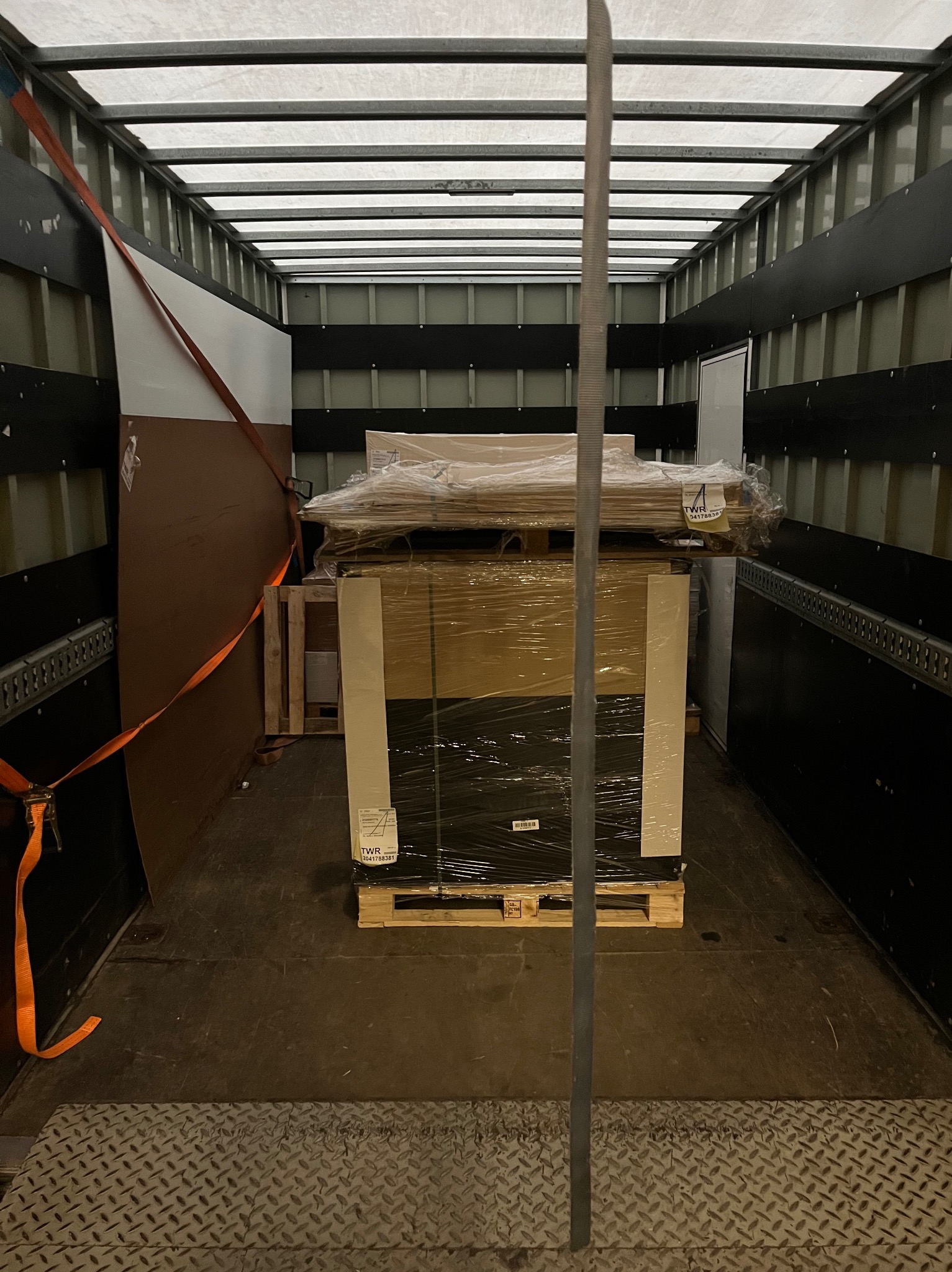 Paleta z towarem zabezpieczona folią i pasami wewnątrz przestrzeni ładunkowej busa. Widoczne elementy mocujące i podłoga z blachy ryflowanej.