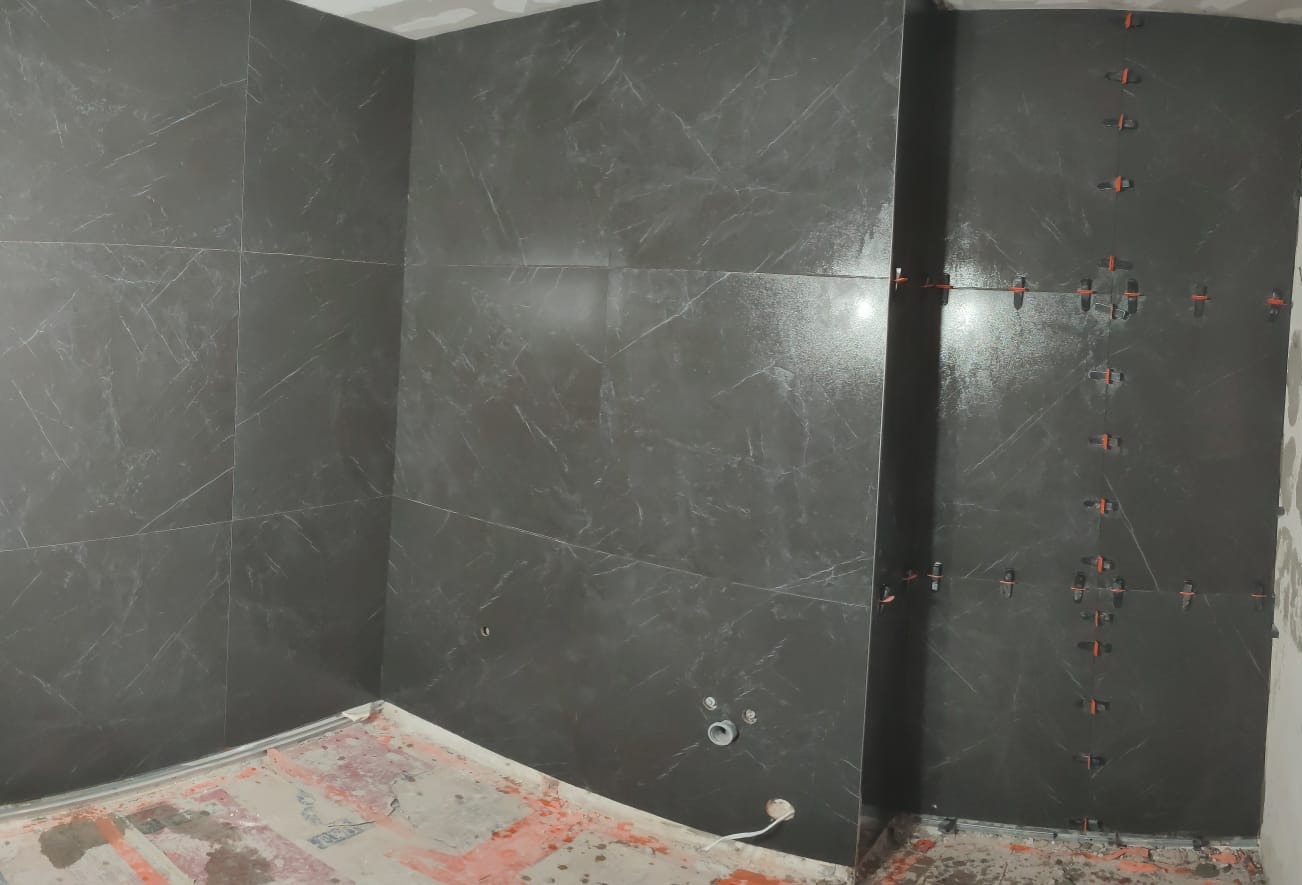 Ciemne, marmurowe płytki ścienne w trakcie montażu w łazience. Widoczne krzyżyki dystansowe i fragment podłogi przed wykończeniem. Ujęcie z narożnika.