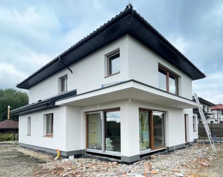 Nowoczesny dom jednorodzinny z białą elewacją w Bielsku-Białej. Widoczne duże okna i ciemna podbitka dachowa. Elewacja świeżo po wykonaniu, teren wokół uporządkowany.