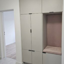 Mistrzowski Wymiar - Nowoczesna, pełnowymiarowa szafa modułowa w przedpokoju, z jasnoszarymi frontami, czarnymi uchwytami i wbudowaną wnęką z różowym siedziskiem.