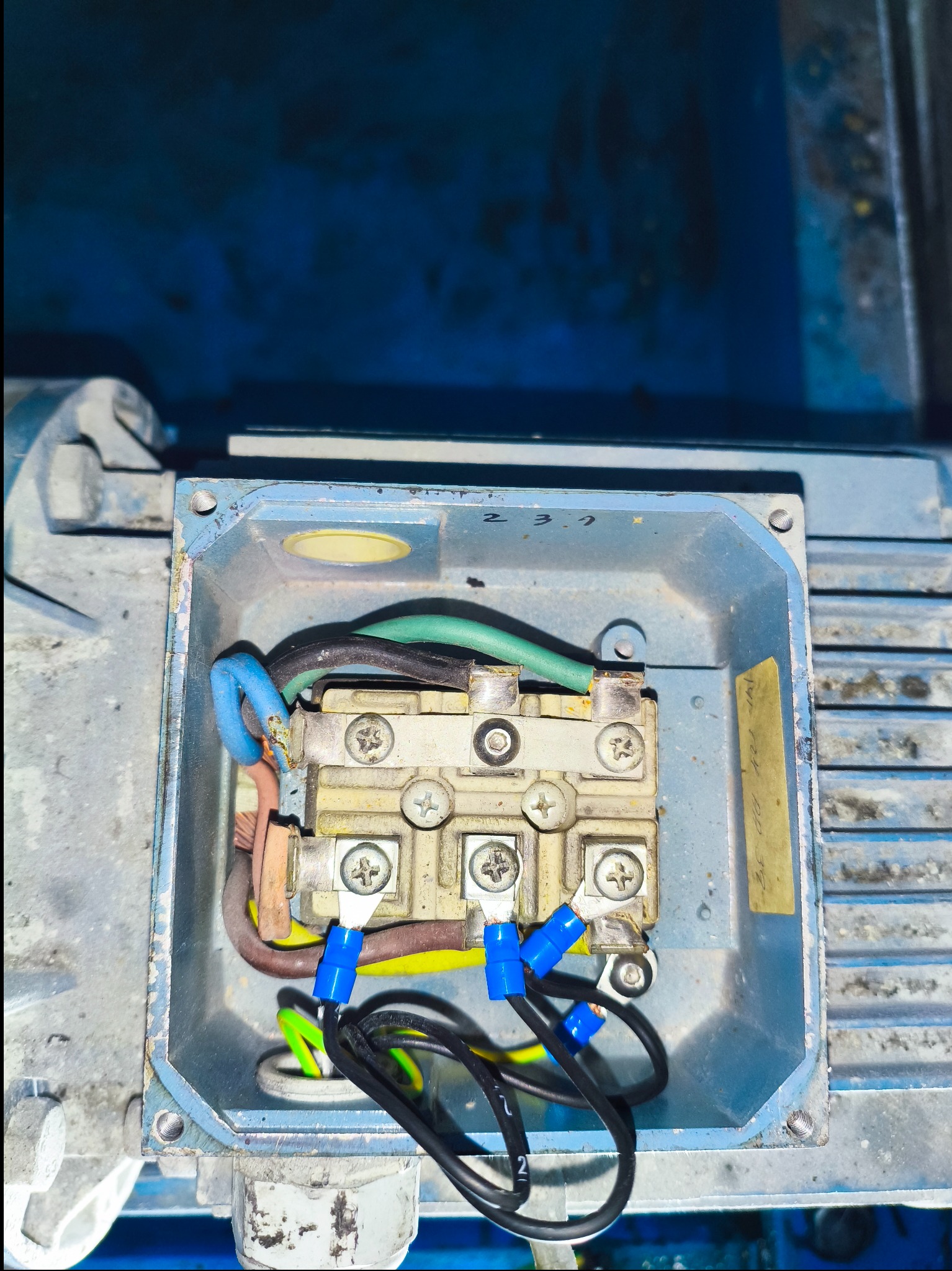 Szczegółowe ujęcie skrzynki przyłączeniowej silnika elektrycznego z widocznymi przewodami o różnych kolorach i złączkami, w metalowej obudowie.