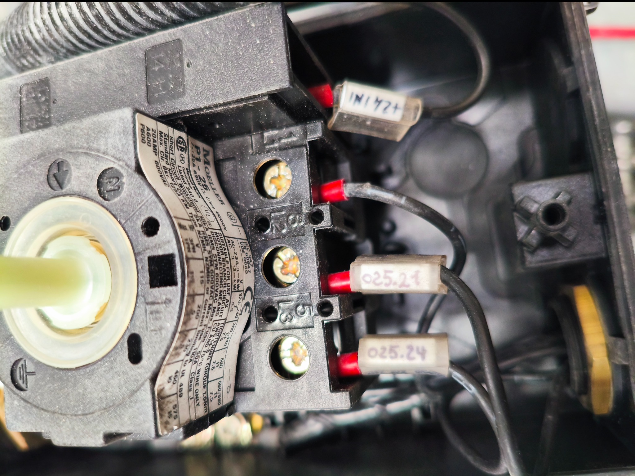 Szczegółowe ujęcie podłączeń elektrycznych wewnątrz czarnej obudowy, z widocznymi przewodami oznaczonymi etykietami i śrubami mocującymi.