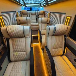 Busem do Celu do Niemiec, Holandii i Belgii, a także powroty do Polski z tych krajów - Luksusowe wnętrze busa z beżowymi skórzanymi fotelami, oświetleniem LED na suficie i podłodze, tworzące ekskluzywną atmosferę. Widok na komfortowe siedzenia i detale wykończenia.