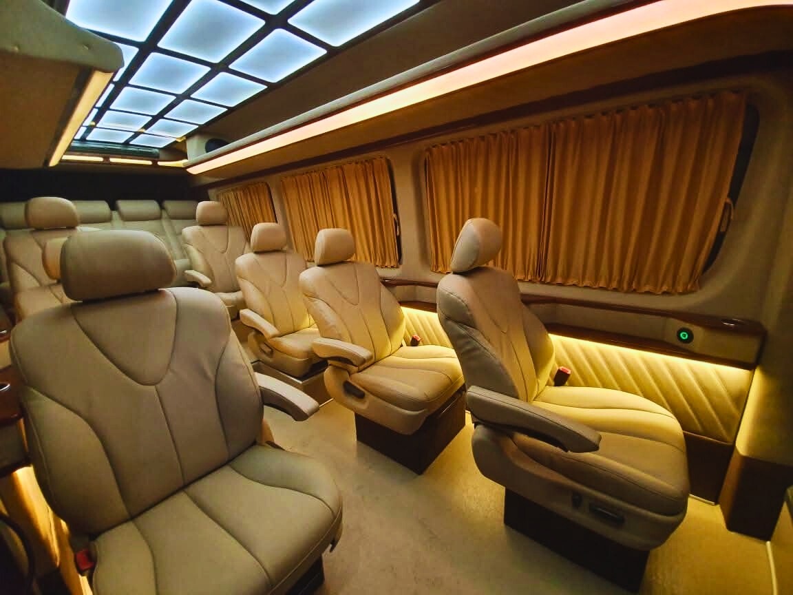 Luksusowe wnętrze busa w Warszawie: beżowe skórzane fotele z zagłówkami, oświetlenie LED podsufitki i boczne, zasłony w oknach, komfortowe warunki podróży.