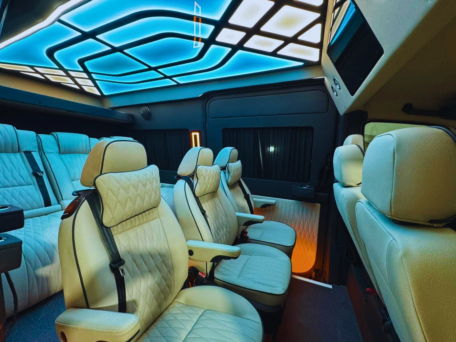 Luksusowe wnętrze busa z kremowymi skórzanymi fotelami, oświetleniem LED na suficie i zasłonami w oknach, ukazujące komfort i elegancję podróży.