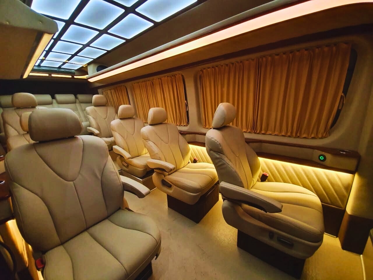 Luksusowy bus z beżowymi skórzanymi fotelami, oświetleniem LED i zasłonami w oknach, wnętrze pojazdu z perspektywy pasażera.