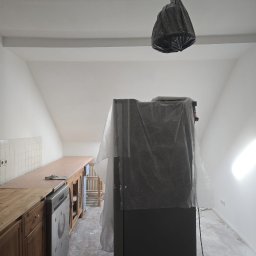 Sebastian Łachowski - Kuchnia w trakcie remontu: meble zabezpieczone folią, sufit i ściany świeżo pomalowane na biało, podłoga częściowo zakryta. Lampa owinięta folią ochronną.