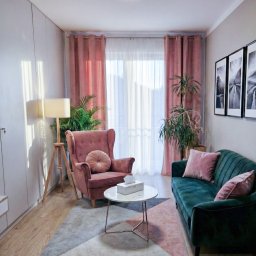 INTROS SPÓŁKA Z OGRANICZONĄ ODPOWIEDZIALNOŚCIĄ - Przytulny gabinet terapeutyczny: fotel uszak, zielona sofa z poduszkami, marmurowy stolik, lampa na trójnogu, obrazy na ścianie i rośliny doniczkowe.