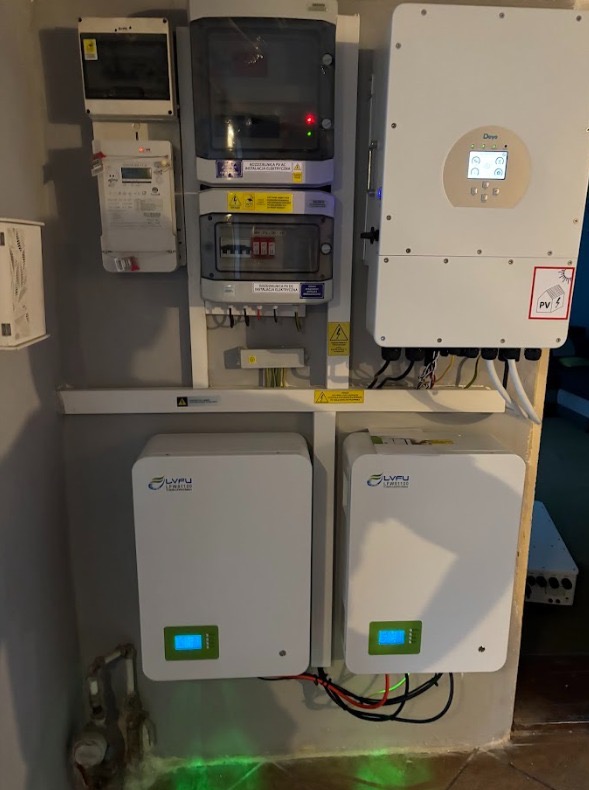 Kompletna instalacja fotowoltaiczna wewnątrz budynku: inwerter, akumulatory energii LVFU, rozdzielnia elektryczna i liczniki. Widoczne okablowanie i elementy montażowe.