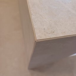 Jakub Frączek Wykończenia Wnętrz - Beżowa, marmurkowa płyta ceramiczna, widoczny narożnik i krawędź. Delikatna faktura kamienia, ciepłe odcienie beżu. Minimalistyczny detal wykończenia wnętrza.