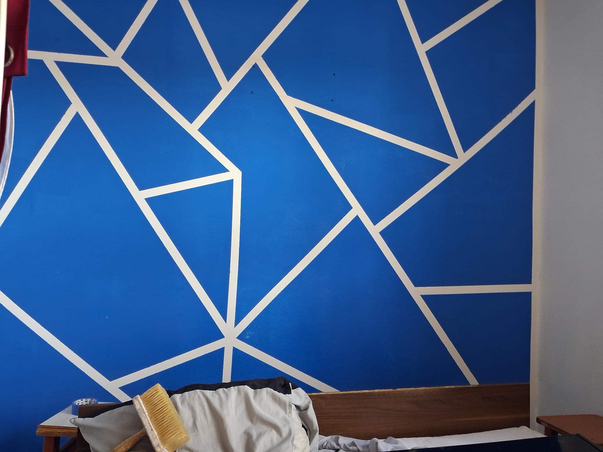 Niebieska ściana z geometrycznym wzorem w bieli, świeżo po malowaniu w Bystrzycy. Widoczny pędzel i fragment mebli, co sugeruje domowe otoczenie.