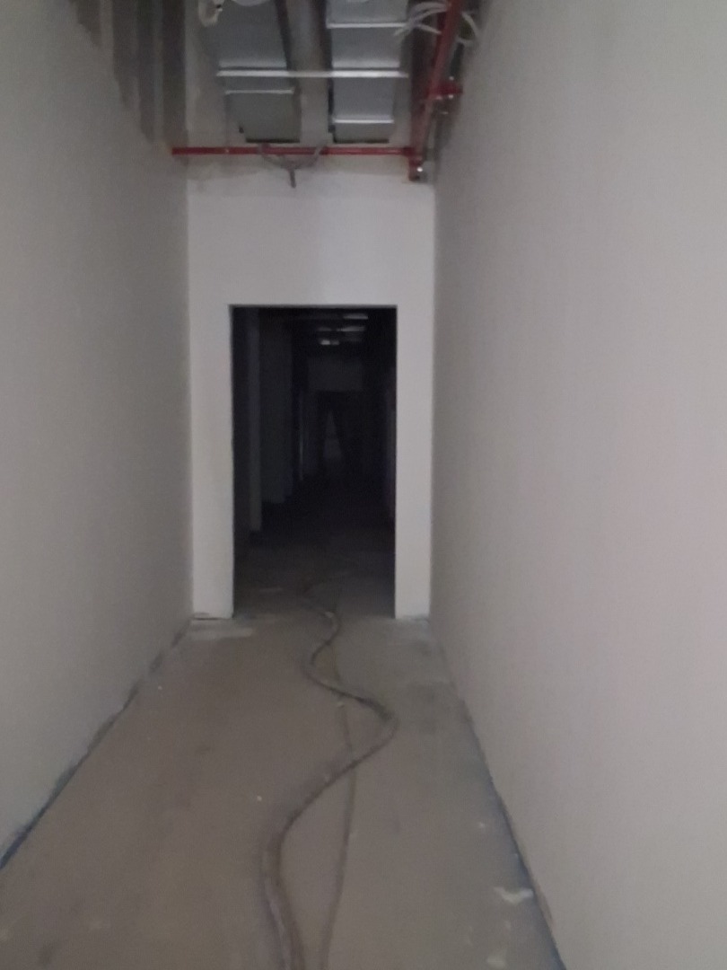 Korytarz w trakcie prac wykończeniowych: świeżo pomalowane ściany w odcieniach szarości, widoczne instalacje pod sufitem i kabel na podłodze. Surowy stan.