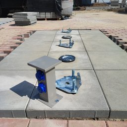 HYDRO ABS mgr inż. Bartosz Siwiec - Montaż oświetlenia i gniazd elektrycznych w kostce brukowej. Widoczne elementy instalacji przed ostatecznym wykończeniem. Jasne, dzienne światło.