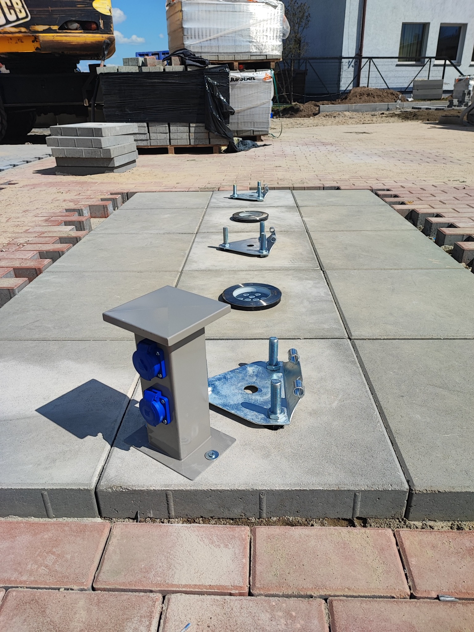 Montaż oświetlenia i gniazd elektrycznych w kostce brukowej. Widoczne elementy instalacji przed ostatecznym wykończeniem. Jasne, dzienne światło.