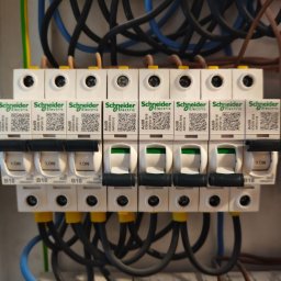 ElektrykSpecOk - Rozdzielnica elektryczna Schneider Electric z widocznymi bezpiecznikami i przewodami. Część wyłączników jest w pozycji 'ON'.