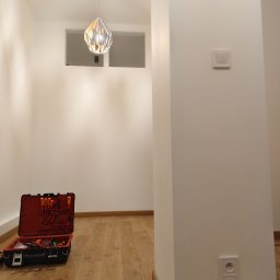 ElektrykSpecOk - Nowoczesne wnętrze z zamontowaną lampą wiszącą. Otwarta skrzynka z narzędziami elektrycznymi obok ściany z gniazdkami i włącznikiem. Minimalistyczny design.