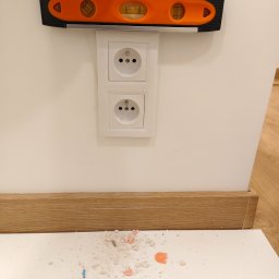 ElektrykSpecOk - Poziomica przykładana do gniazdka elektrycznego podwójnego, białe gniazdko na białej ścianie, widoczne ślady po montażu.