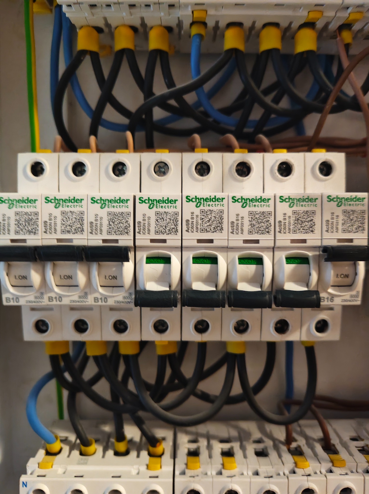 Rozdzielnica elektryczna Schneider Electric z widocznymi bezpiecznikami i przewodami. Część wyłączników jest w pozycji 'ON'.