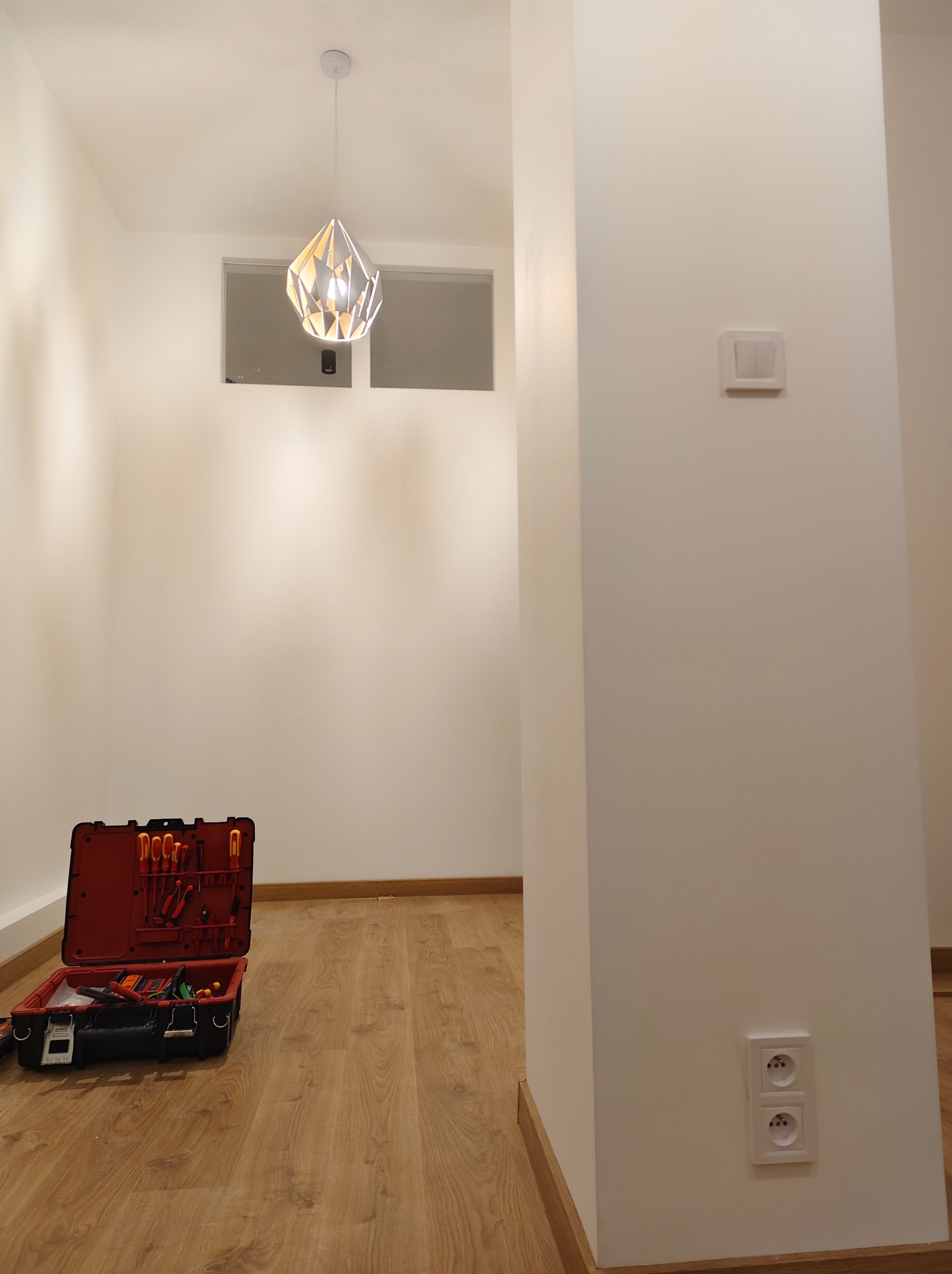 Nowoczesne wnętrze z zamontowaną lampą wiszącą. Otwarta skrzynka z narzędziami elektrycznymi obok ściany z gniazdkami i włącznikiem. Minimalistyczny design.