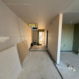 Sławomir Wojtuń - Korytarz w trakcie montażu płyt gipsowo-kartonowych na ścianach i suficie. Widoczna drabina, narzędzia i instalacje elektryczne. Surowy stan wykończenia.
