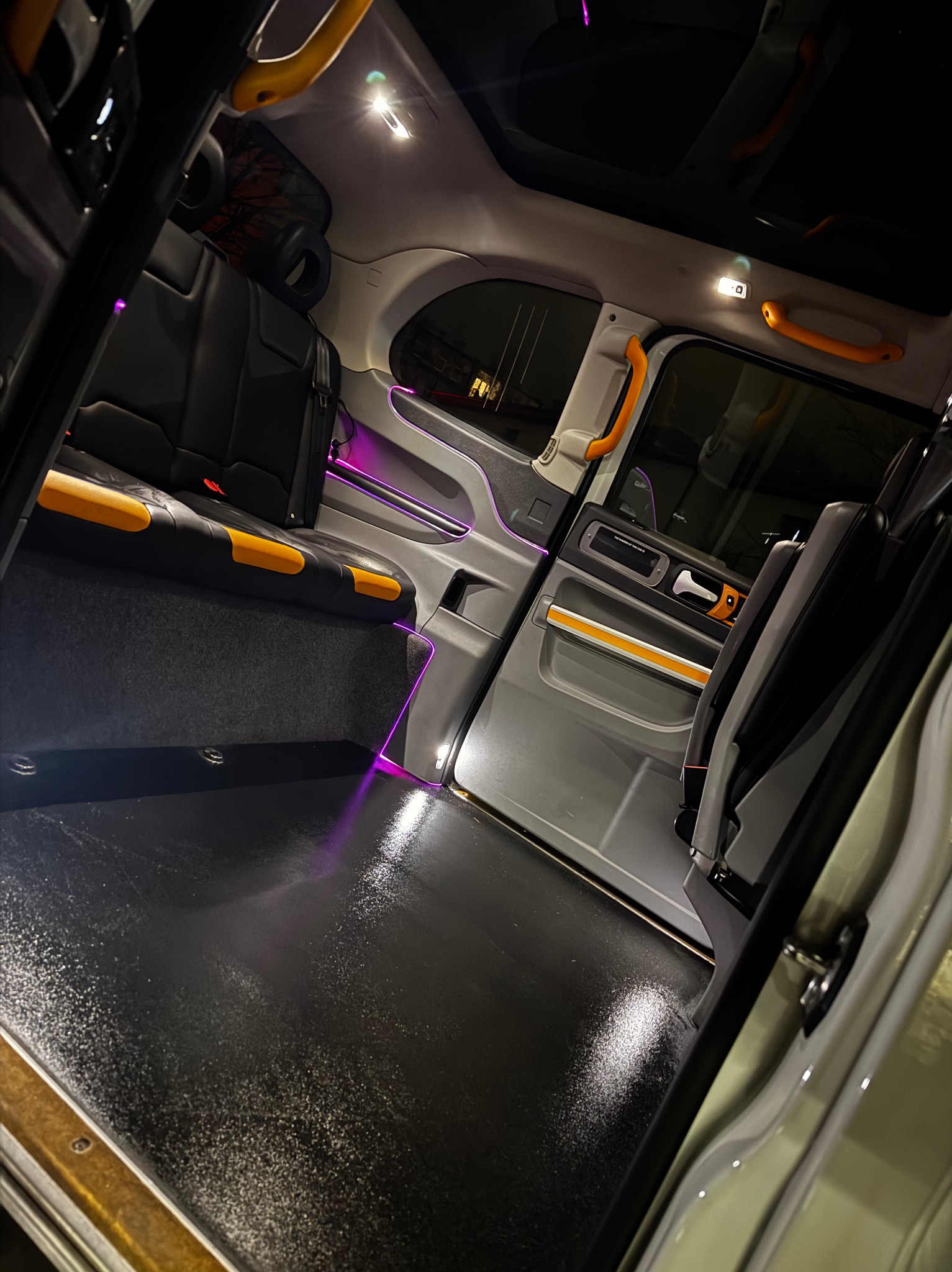 Wnętrze taksówki z czarnymi skórzanymi siedzeniami z żółtymi akcentami i fioletowym oświetleniem LED, widok z perspektywy pasażera, czarna podłoga.