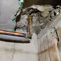 HYDROTOMI TOMASZ OSTAŁOWSKI - Miedziana rura z zaworem w ścianie z siatką w Warszawie. Widoczne ślady po kuciu i zaprawie. Instalacja po naprawie lub w trakcie przeróbki.