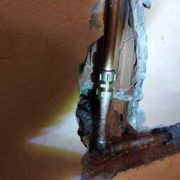 HYDROTOMI TOMASZ OSTAŁOWSKI - Miedziane rury połączone złączką w wykuciu ściany. Widoczne ślady po naprawie instalacji. Ujęcie z bliska, oświetlenie punktowe.