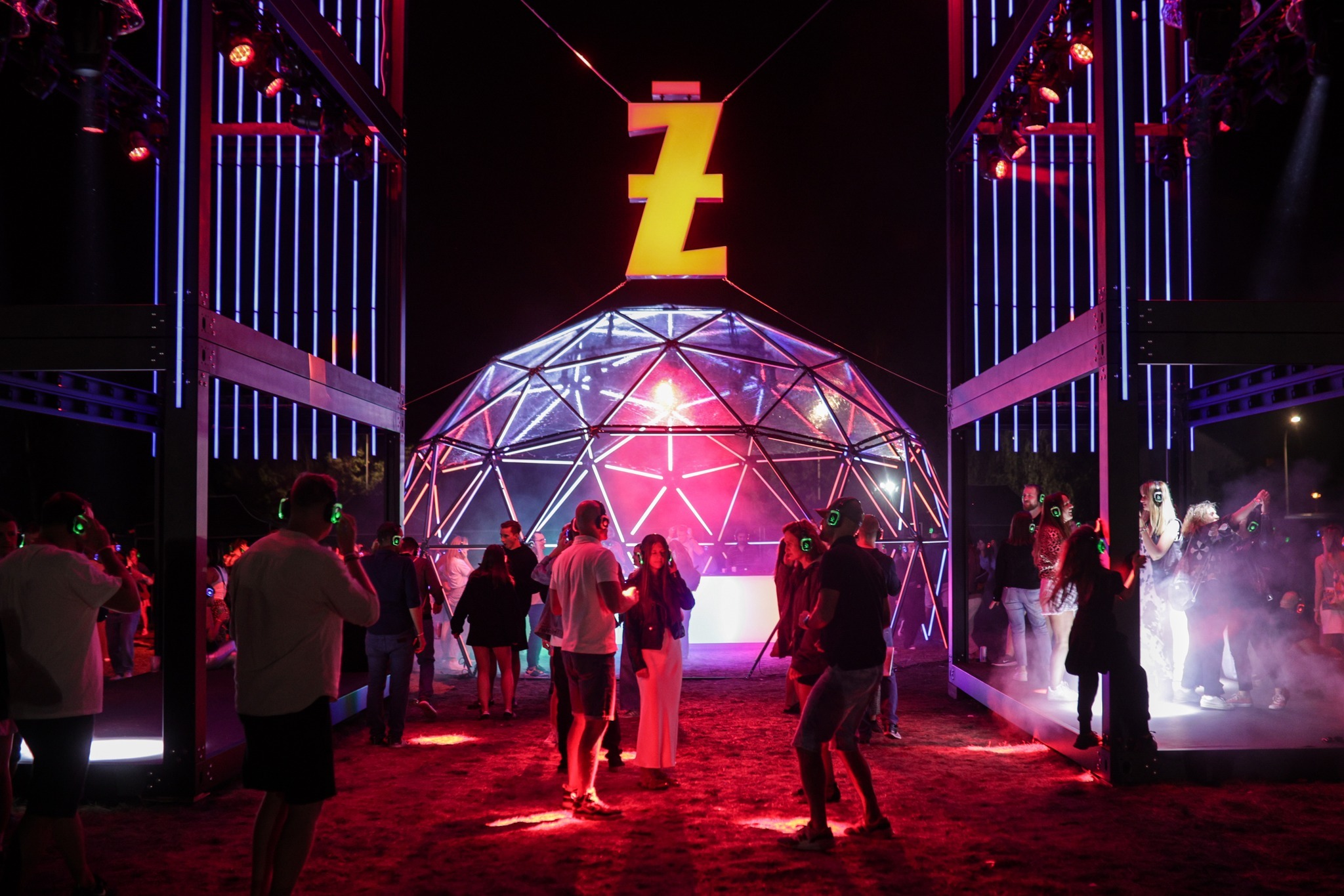 Nocna impreza silent disco z kopułą oświetloną neonami i uczestnikami w słuchawkach. Scena z logo 'Z' i dekoracje świetlne tworzą unikalny klimat wydarzenia.