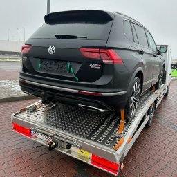 Jakub Piekarski - Czarny SUV Volkswagen Tiguan 2.0 TDI eMotion, zabezpieczony pasami, transportowany na srebrnej lawecie z aluminiową platformą. Widok z tyłu, pochmurne niebo w tle.