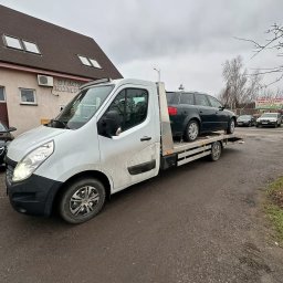 Jakub Piekarski - Biała laweta Renault Master z załadowanym ciemnym kombi Audi na platformie, zaparkowana na placu przed budynkiem w pochmurny dzień. Widoczny znak 'DIAGNOSTYKA KOMPUTEROWA'.