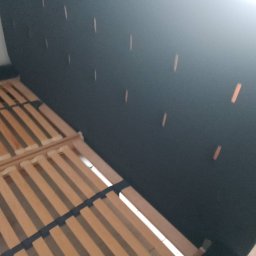 MS Glamour Usługi tapicerskie - Tapicerowane wezgłowie łóżka w kolorze grafitowym z drewnianym stelażem. Widoczne zszywki na materiale. Ujęcie z bliska, ukazujące detale wykończenia.